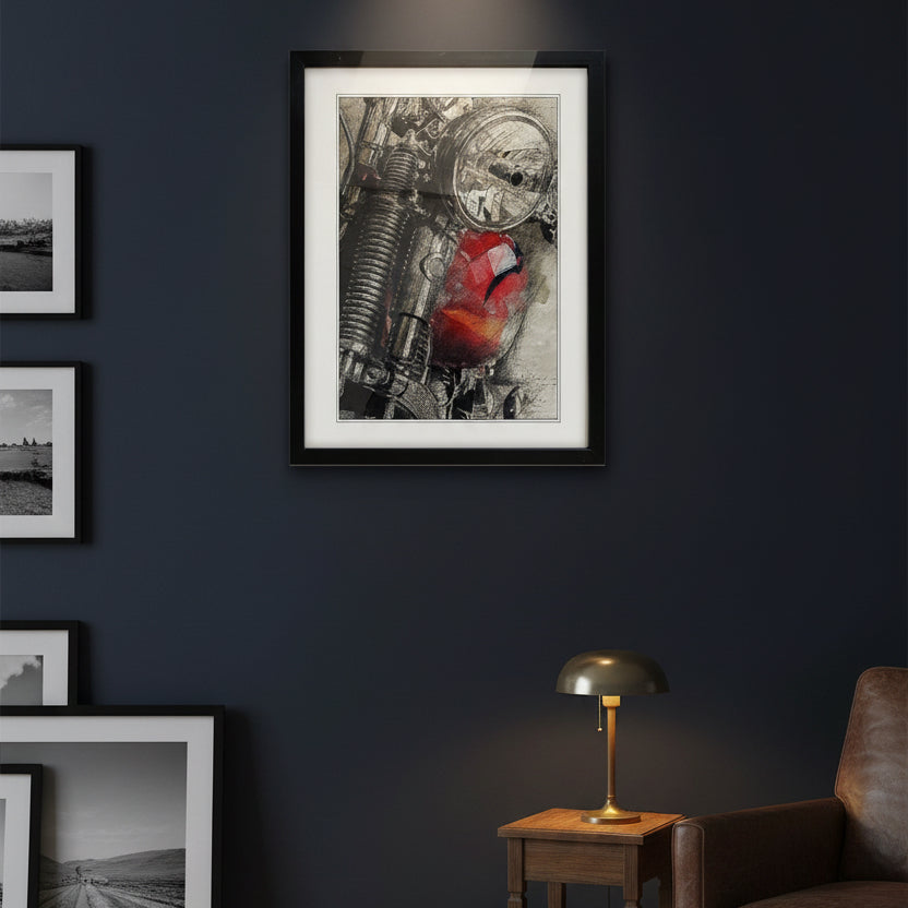 A framed art print featuring a close-up of a motorcycle engine with a vibrant red paint splatter, displayed on a dark blue wall above a gray armchair and a small wooden side table.
