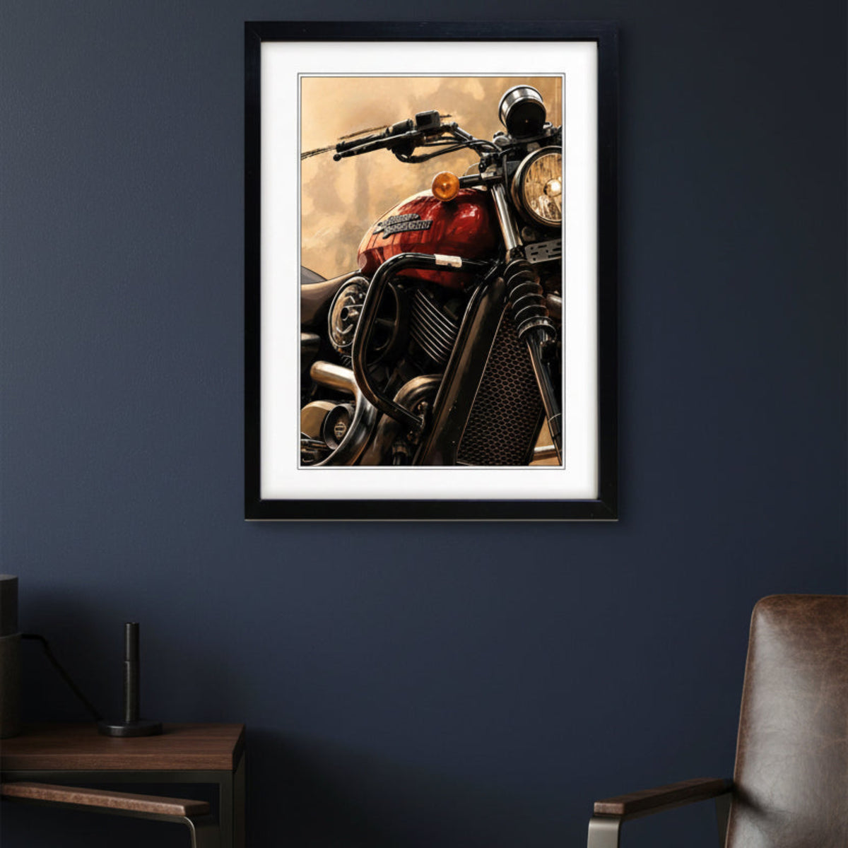 A framed wall art print featuring a close-up motorcycle photograph with a red fuel tank, black frame, and warm beige background, displayed on a dark navy wall above a wooden side table and chair.