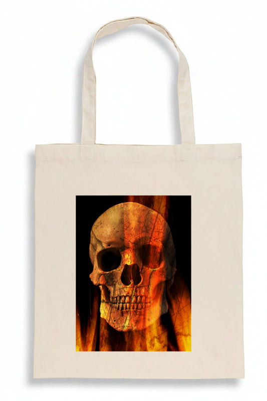 A cream-colored canvas tote bag featuring a square graphic print of a skull overlaid with orange and yellow flames on a black background.