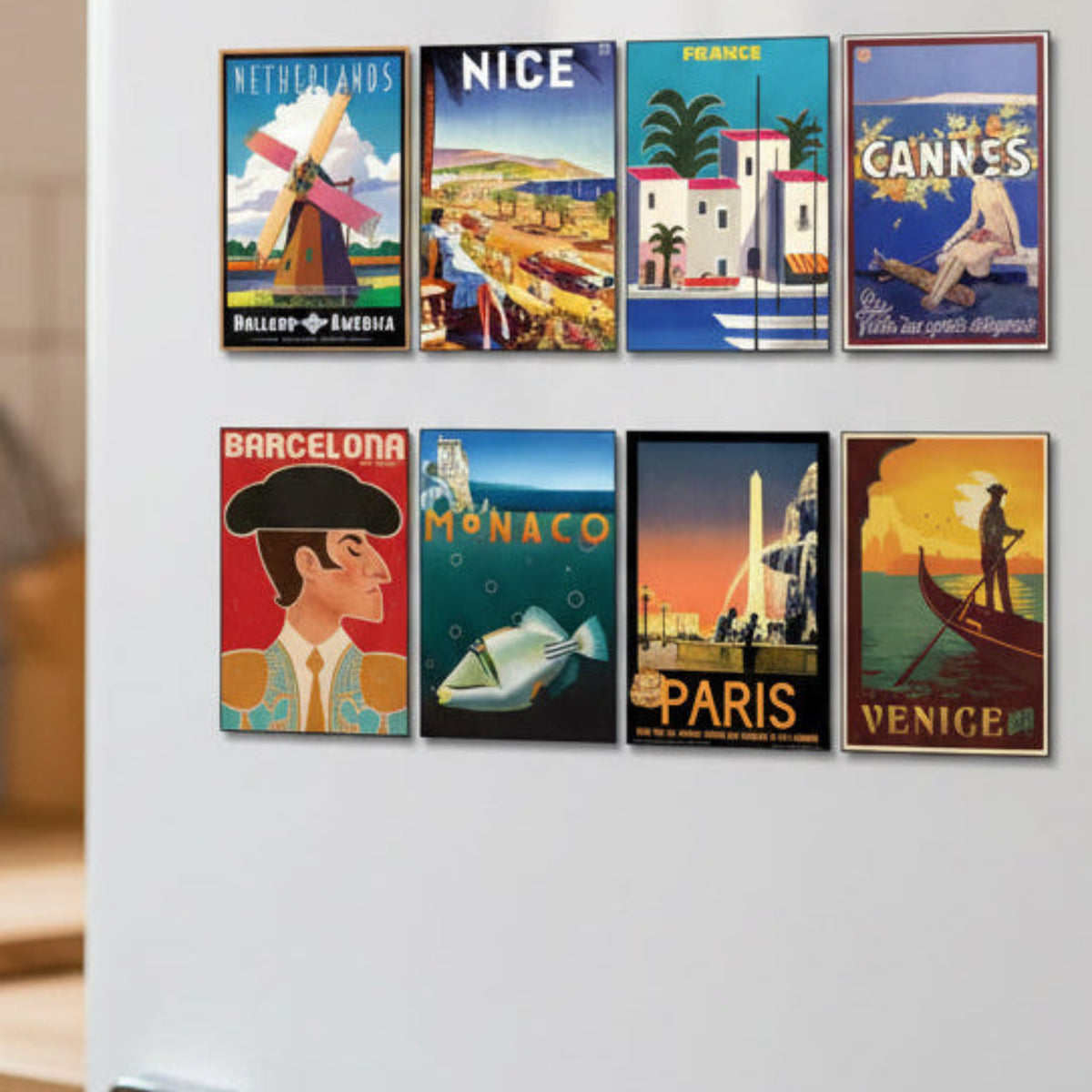 A set of eight framed travel posters showcasing different European destinations including Netherlands, Nice, France, Cannes, Barcelona, Monaco, Paris, and Venice, arranged in two rows on a gray background.