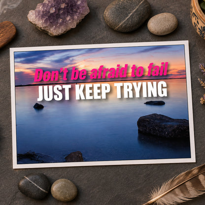 A motivational quote graphic reading 'Don't be afraid to fail JUST KEEP TRYING' in pink and white text over a calm lake landscape at dusk with rocks in the foreground.