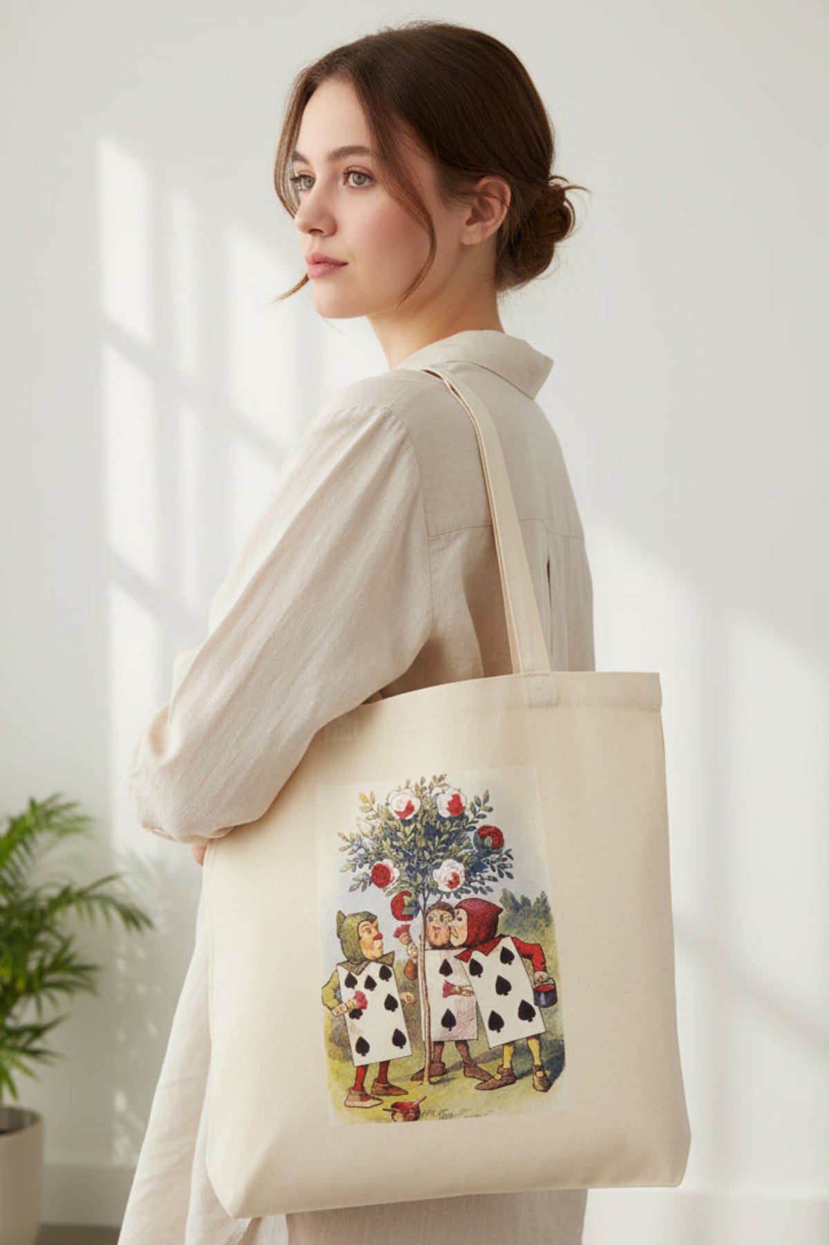 A natural canvas tote bag with a printed illustration of two children dressed as playing cards under a tree of red apples, shown against a plain white background.