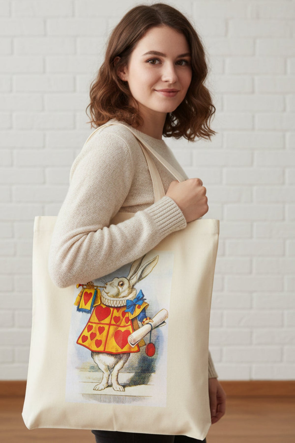 A natural canvas tote bag featuring a printed illustration of the White Rabbit in a red and yellow heart-patterned jacket, holding a small bag and a scroll.