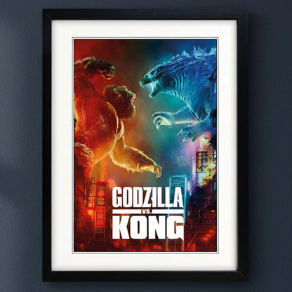 A framed Godzilla vs Kong movie poster featuring King Kong and Godzilla facing off in a city scene, with the title 'Godzilla vs Kong' in large white text at the bottom. The poster is mounted with a white mat inside a black frame, shown against a dark gray wall.
