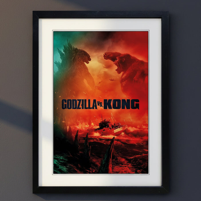 Framed wall art poster featuring a dramatic Godzilla vs Kong battle scene, with Godzilla on the left in dark teal tones and Kong on the right in fiery red-orange tones, shown in a black frame with white mat on a light gray background.