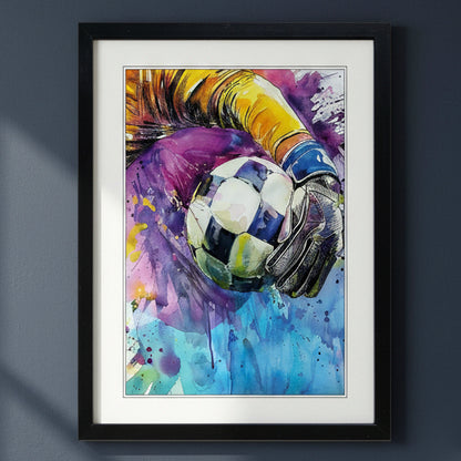 Framed watercolor art print of a soccer goalkeeper in action, featuring a vibrant splash of purple, blue, yellow, and white paint with a black frame and white mat, displayed on a dark gray wall.