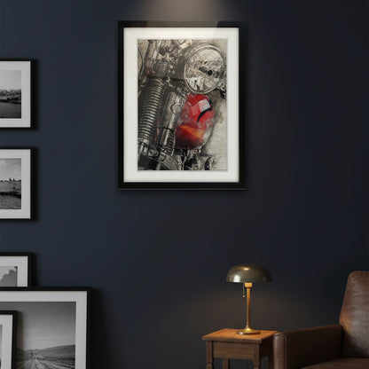 A framed art print featuring a close-up of a motorcycle engine with a vibrant red paint splatter, displayed on a dark blue wall above a gray armchair and a small wooden side table.
