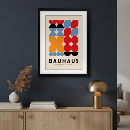 A framed Bauhaus poster featuring a mid-century modern geometric design with red, orange, blue, black, and beige shapes, enclosed in a black frame with a white mat.
