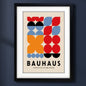 A framed Bauhaus poster featuring a mid-century modern geometric design with red, orange, blue, black, and beige shapes, enclosed in a black frame with a white mat.