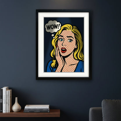 A framed pop-art print featuring a blonde woman with a halftone dot pattern, a speech bubble that says 'WOW!', and a red polka-dot background, shown in a black frame against a white wall.