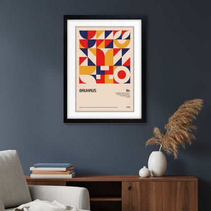 A framed Bauhaus art print featuring a bold geometric pattern in red, yellow, and navy blue on a beige background, enclosed in a black frame with a white mat.