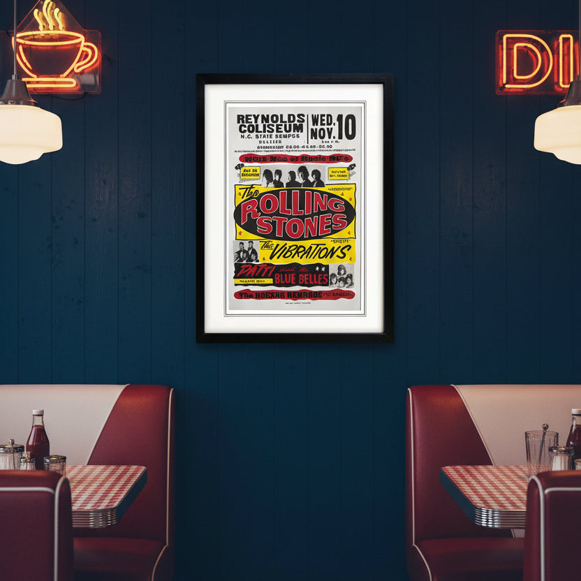 A framed vintage concert poster for The Rolling Stones featuring a black frame, white mat, and a poster with bold red, yellow, and black text on a light gray background.