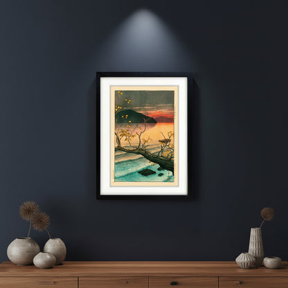 A framed Japanese-style art print depicting a sunset over a calm lake with a dark mountain, a fallen tree branch with yellow leaves, and blue water, shown in a black frame with a white mat on a white background.