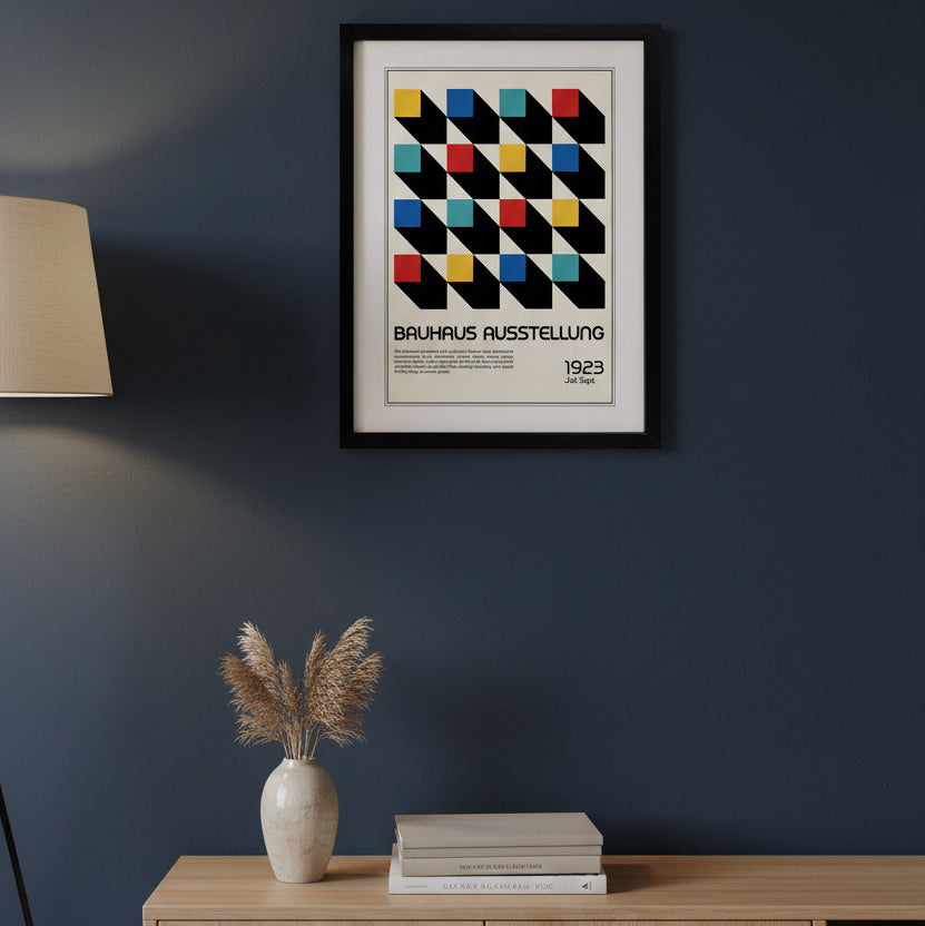 A framed Bauhaus exhibition poster print featuring a geometric pattern of black diagonal blocks with colored squares in yellow, red, blue, and teal on an off-white background, enclosed in a black frame with a white mat.