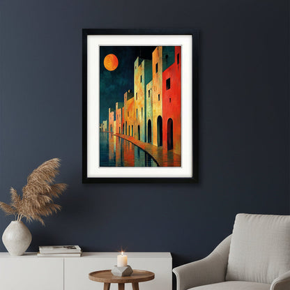 Framed art print featuring a colorful painting of Mediterranean-style buildings along a waterfront at night, with a large orange moon in the sky and reflections in the water, shown in a black frame with a white mat.