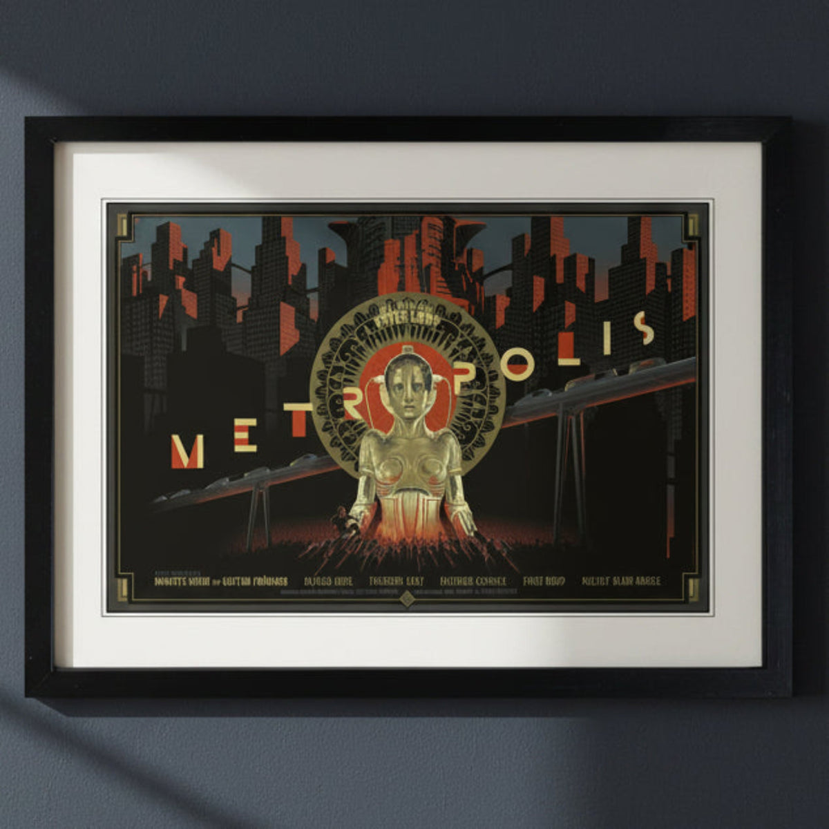 A framed art print featuring a stylized Metro-polis cityscape poster design with a central robot figure, shown in a black frame with a white mat against a light gray background.