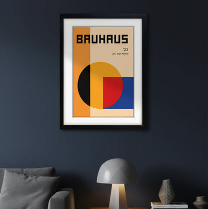 A framed Bauhaus '23 art print featuring a minimalist geometric design with orange, beige, yellow, red, and blue blocks, presented in a modern apartment with minimalistic furniture.