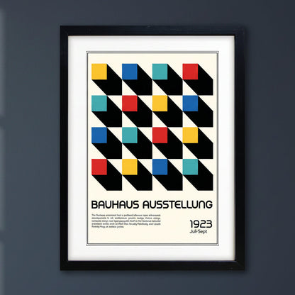 A framed Bauhaus exhibition poster print featuring a geometric pattern of black diagonal blocks with coloured squares in yellow, red, blue, and teal on an off-white background, The black framed Print is in a dark blue background or wall with natural lighting.