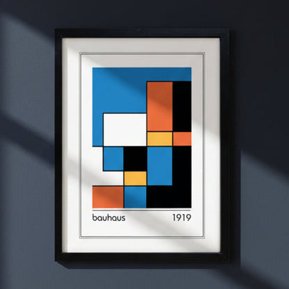 Framed Bauhaus 1919 abstract geometric art print featuring a grid of blue, orange, yellow, black, and white blocks, presented in a black frame on a dark blue wall.