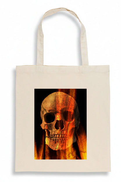 A cream-colored canvas tote bag featuring a square graphic print of a skull overlaid with orange and yellow flames on a black background.