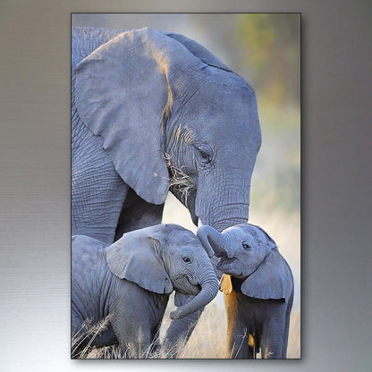 A vertical photographic print of three gray elephants in a natural grassy setting, shown hanging against a gray wall.