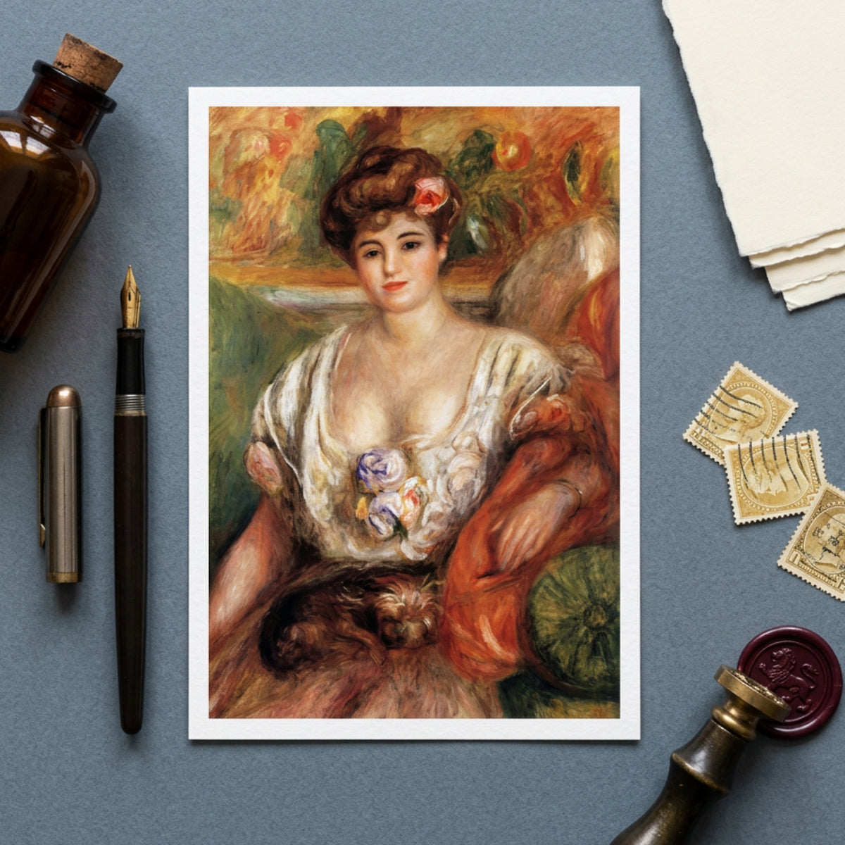 A framed art print of a classic impressionist portrait of a woman with a cat, styled in a flat-lay on a slate blue background with vintage props including a bottle, fountain pen, stamps, and wax seal.