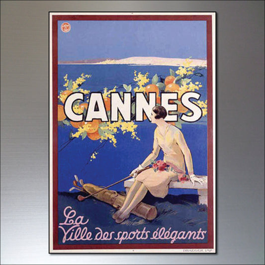 A vintage-style poster print fridge magnets featuring a woman seated by the sea with large white text reading 'CANNES' and smaller script text 'La Ville des sports élégants' on a blue background with yellow floral accents.