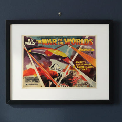 Framed vintage movie poster for H.G. Wells war of the worlds movie promotion hung in a black frame on a dark blue wall 
