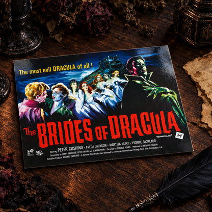 A vintage movie poster for 'The Brides of Dracula' resting on a wooden tabletop. The poster features classic horror artwork with Dracula in the foreground and the cast listed at the bottom, including Peter Cushing, Freda Jackson, and others.