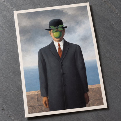 A surreal portrait of a man in a dark overcoat, white shirt, and orange tie, wearing a black bowler hat with green leaves and a green fruit over his eyes, set against a cloudy sky and stone wall.