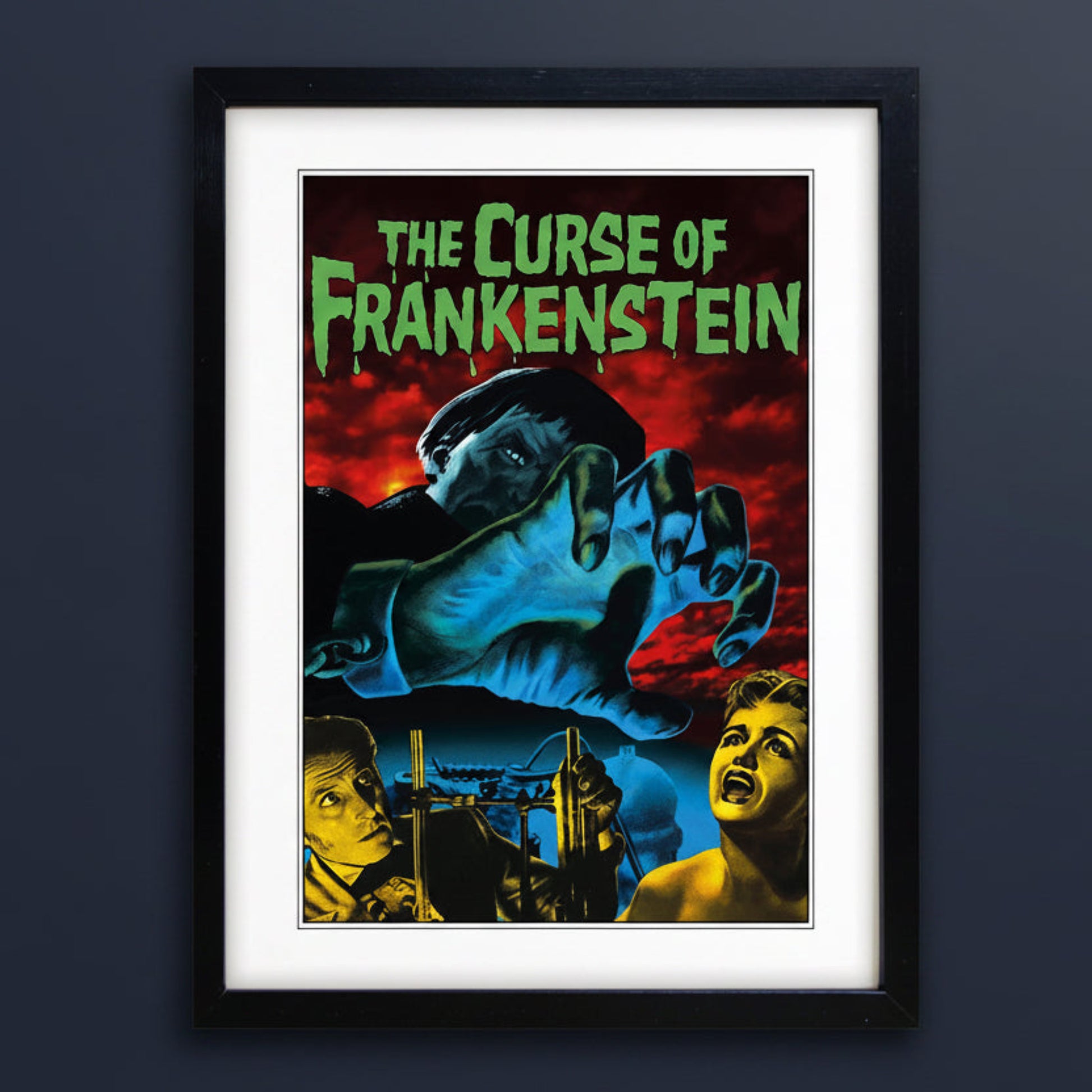 Framed vintage-style poster for 'The Curse of Frankenstein' with a black frame, white mat, and a dramatic illustration featuring a giant blue hand, red sky, and green title text.