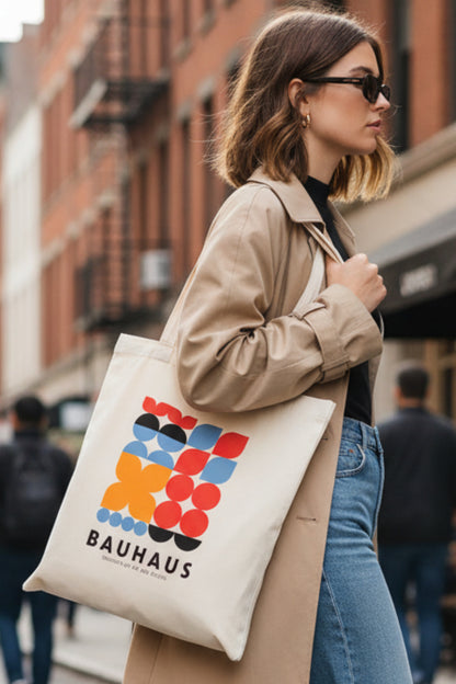 A cream-colored canvas tote bag featuring a colorful Bauhaus geometric logo print in red, orange, blue, black, and white, with the text 'BAUHAUS INSTITUTE OF ART AND DESIGN' printed below.