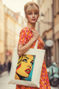 A cream-colored canvas tote bag featuring a colorful pop-art graphic of a woman's face on the front, set against a plain white background.
