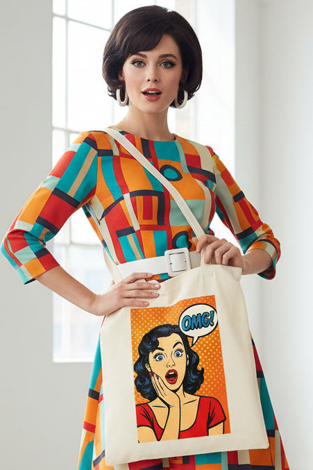 A cream-colored canvas tote bag featuring a retro pop-art graphic of a surprised woman with a speech bubble that says 'OMG!' on a solid white background.