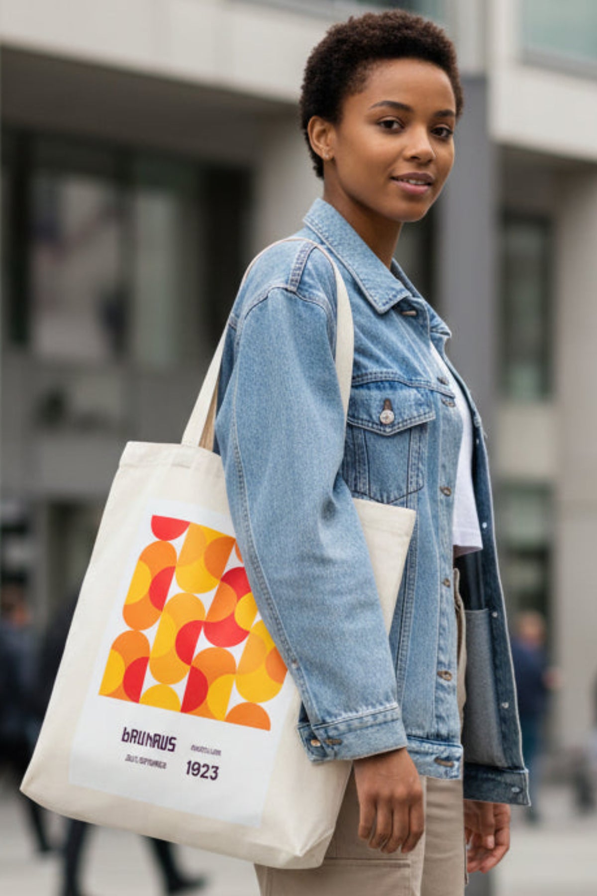 A cream-colored canvas tote bag featuring a retro graphic print with overlapping orange, yellow, and red circles, and text reading 'brauhaus', 'mottellus', '20 09 1923'.