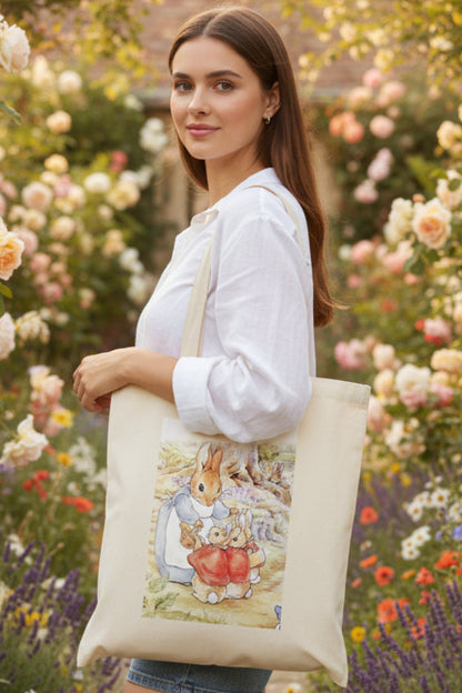 A natural canvas tote bag featuring a printed watercolor illustration of Peter Rabbit and his mother on the front, set against a plain white background.