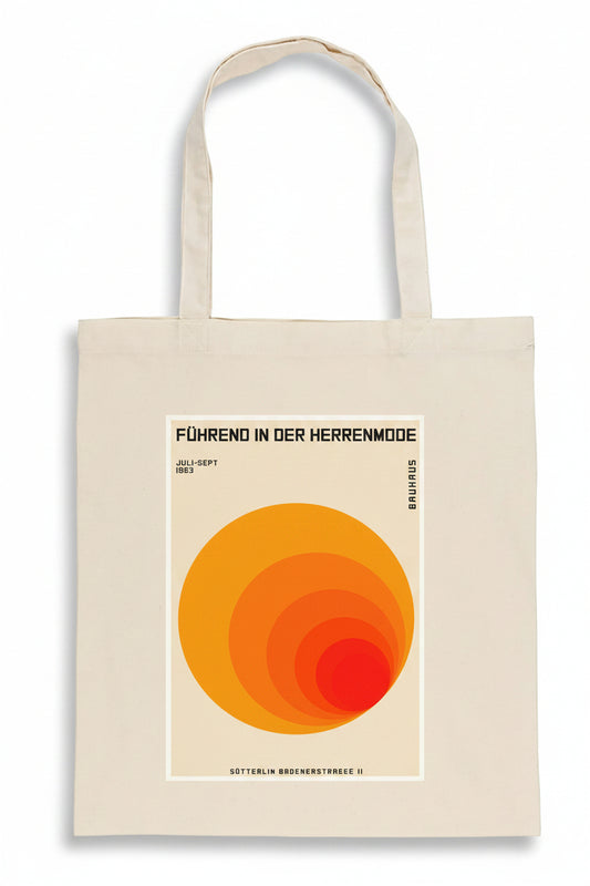 A cream-colored canvas tote bag featuring a retro-style orange and yellow graphic print with German text, displayed against a solid white background.