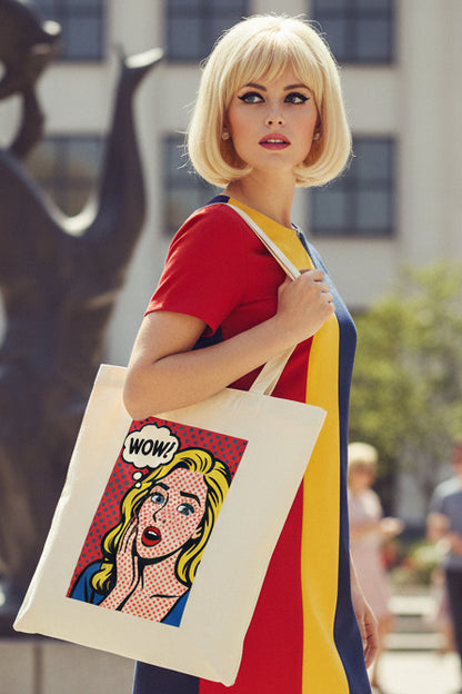 A cream-colored canvas tote bag featuring a pop-art graphic of a surprised blonde woman with a 'WOW!' speech bubble on a red polka-dot background.