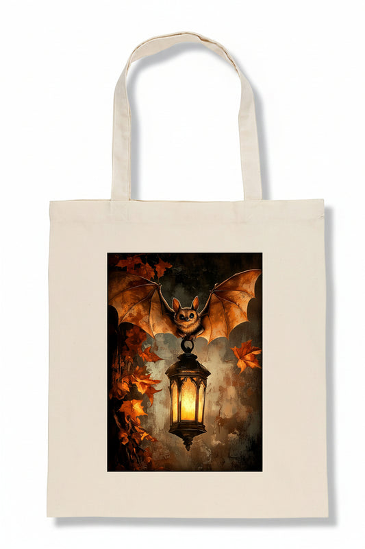 An off-white canvas tote bag with a large rectangular graphic print on the front. The print shows a bat with spread wings holding or beside a glowing lantern, surrounded by dark clouds and orange autumn leaves.