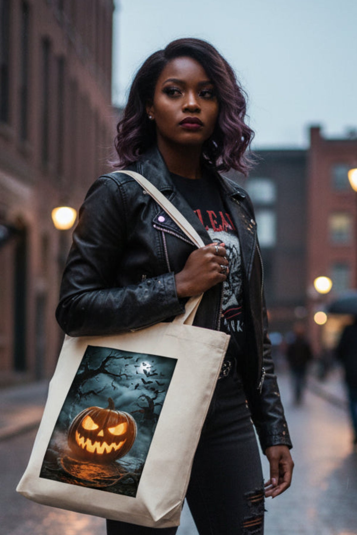 A cream-colored canvas tote bag featuring a rectangular graphic print of a glowing jack-o'-lantern pumpkin in a spooky, dark forest scene with bats and bare trees.