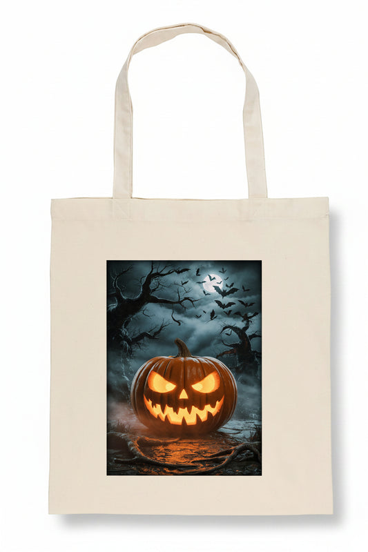 A cream-colored canvas tote bag featuring a rectangular graphic print of a glowing jack-o'-lantern pumpkin in a spooky, dark forest scene with bats and bare trees.
